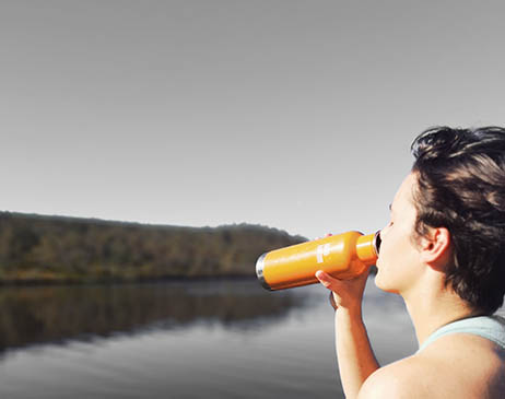 Person drinking water next to a lake